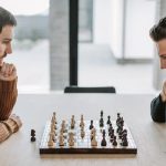 Why Empathy Is the Ultimate Strategic Asset in Creative Leadership Two adults deeply engaged in a strategic chess match on a wooden table indoors.