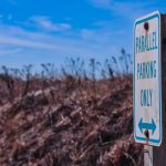 An outdoor parking sign emphasizing parallel parking only, set against a rustic autumn field.
