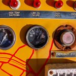 Close-up of a vintage control panel featuring gauges, buttons, and warning labels in a mechanical setting.