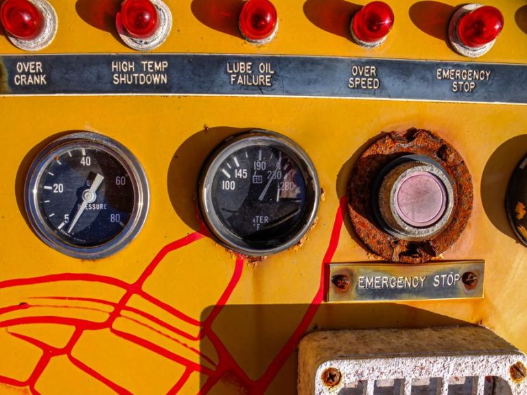 Close-up of a vintage control panel featuring gauges, buttons, and warning labels in a mechanical setting.
