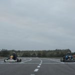 Two athletes racing go-karts on an outdoor racetrack in overcast conditions.