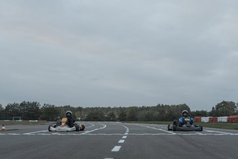 Two athletes racing go-karts on an outdoor racetrack in overcast conditions.