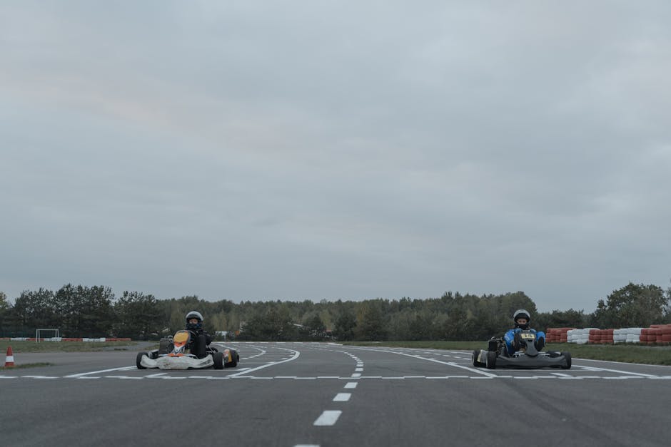 Two athletes racing go-karts on an outdoor racetrack in overcast conditions.