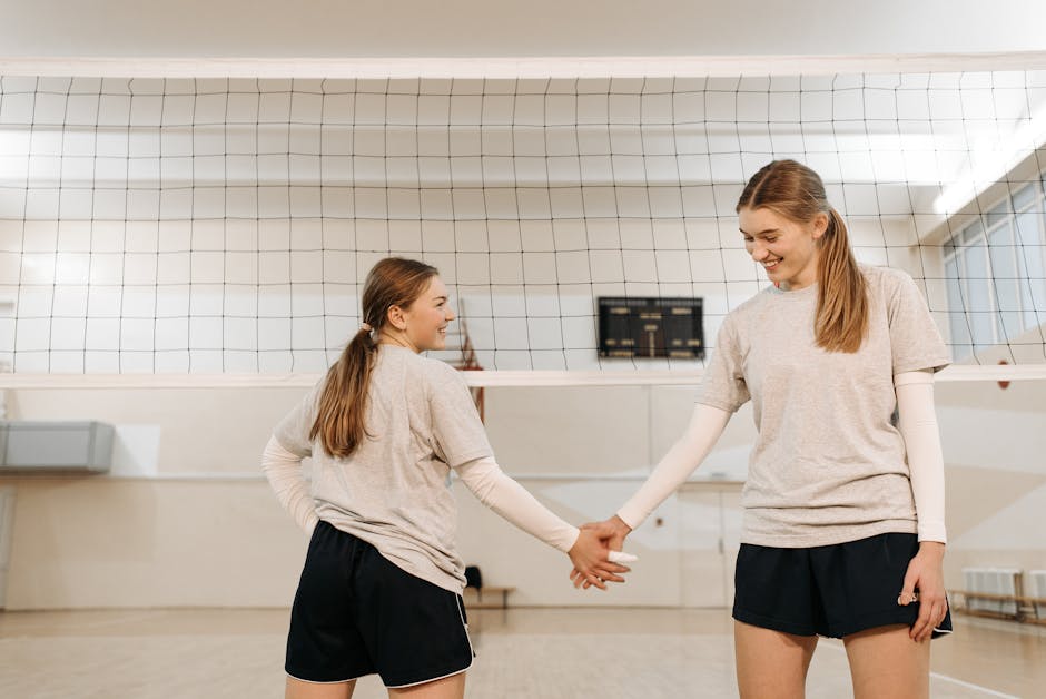 Two female volleyball players smiling and shaking hands over the net, showing teamwork and sportsmanship.
