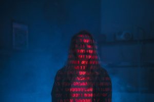 A mysterious silhouette with red binary code projected over the face, set against a dark, moody background.