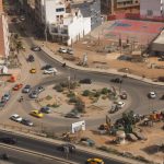 High-angle shot of a busy urban roundabout with vehicles and surrounding buildings.