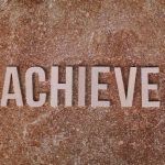 Wooden letters spelling 'ACHIEVE' on a textured brown surface, conveying motivation and success.