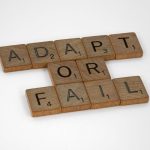 Adaptive Governance Models: Decentralizing for Business Agility Scrabble tiles spell 'Adapt or Fail' on a white background, conveying a motivational message.