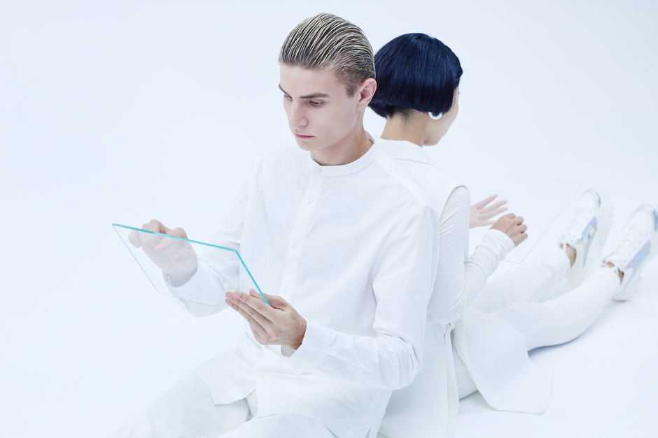 Two adults interacting with transparent tablets, showcasing modern technology in a futuristic white setting.