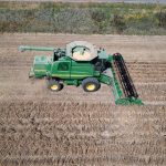 Aerial shot of combine harvester operating in an agricultural field during harvest season.