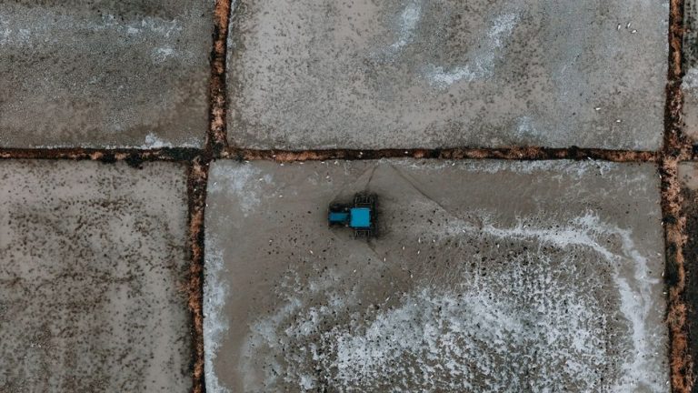 Drone shot of a blue tractor on geometric salt flats, showcasing farming in a unique landscape.