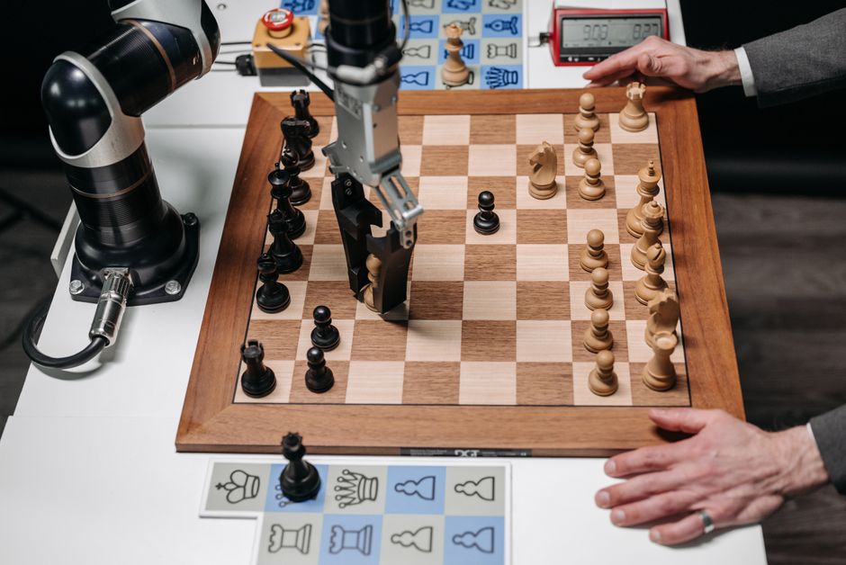 A robotic arm playing chess against a human hand on an electronic chessboard indoors.