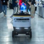 AI-Driven Diplomacy: The Future of High-Stakes Statecraft Autonomous delivery robot navigating indoors during a technology event.