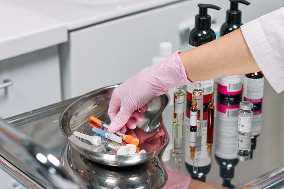 Close-up of a cosmetologist's gloved hand preparing syringes on a tray in a clinic setting.