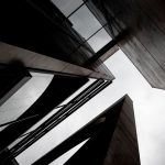Intriguing angle of contemporary skyscrapers with glass and concrete elements against cloudy sky.
