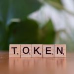 Close-up of Scrabble tiles spelling 'Token' on a wooden surface with a blurred green background.