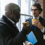 Two diverse professionals in corporate attire having a casual conversation over coffee indoors.