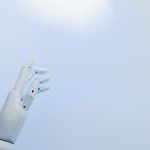 A robotic hand reaching towards a bright light on a white background symbolizing innovation.