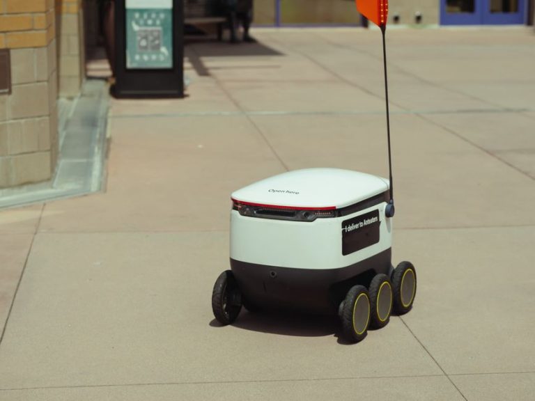 Futuristic autonomous delivery robot navigating a city sidewalk on a sunny day.
