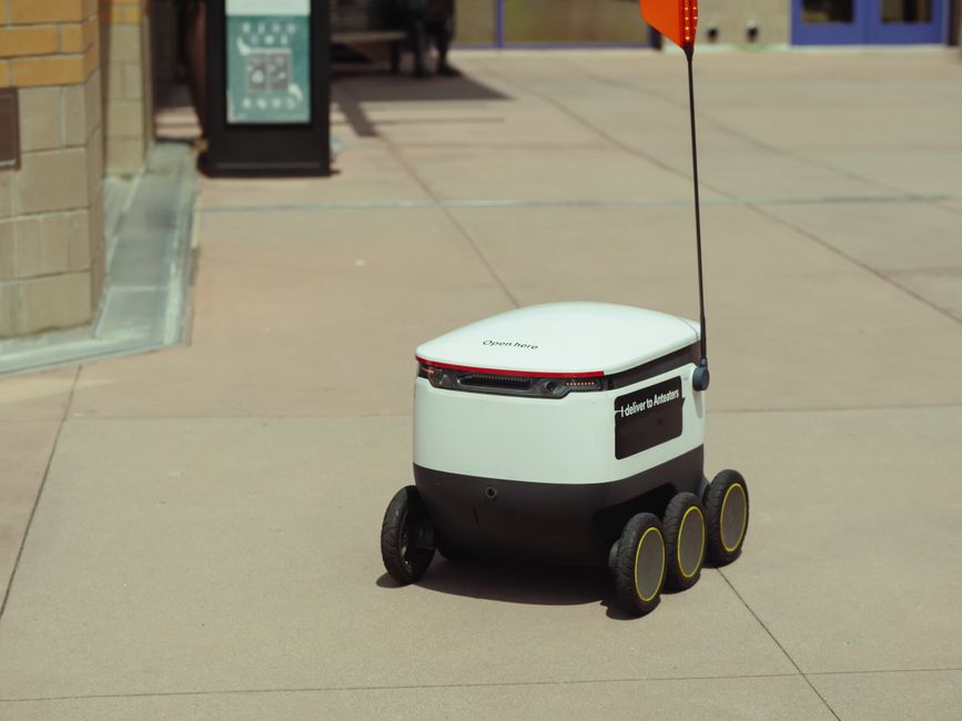 Futuristic autonomous delivery robot navigating a city sidewalk on a sunny day.