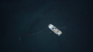 Aerial photograph of a single boat anchored in a vast, dark ocean, captured from above.