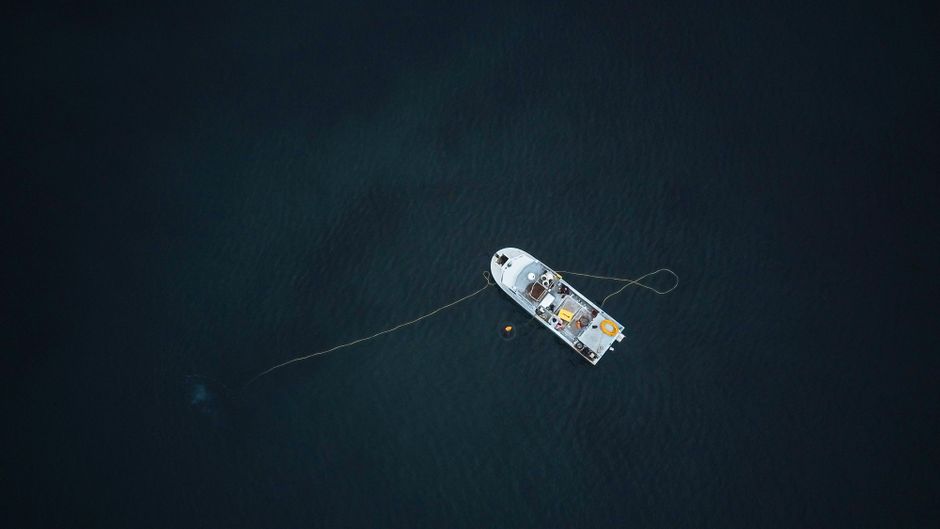 Aerial photograph of a single boat anchored in a vast, dark ocean, captured from above.