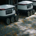 Autonomous Logistics: Scaling Efficiency Without Human Error Futuristic delivery robots navigating a leaf-strewn sidewalk, showcasing innovation in modern urban logistics.