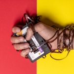 Hand holding tangled cassette tape on vibrant red and yellow background, representing nostalgia.