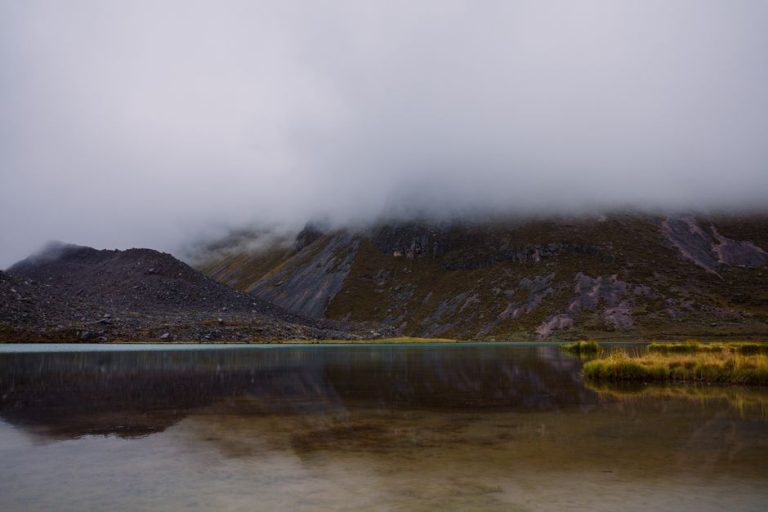 Serene lake with misty mountains in Pajchanta, Peru, reflecting natural beauty.