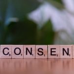 Close-up of Scrabble tiles spelling 'Consent' on a wooden surface, focusing on ethics and communication.