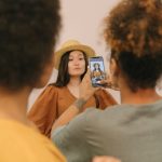 Model posing in a studio as an assistant takes a picture using a smartphone.