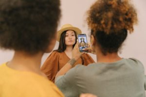 Model posing in a studio as an assistant takes a picture using a smartphone.