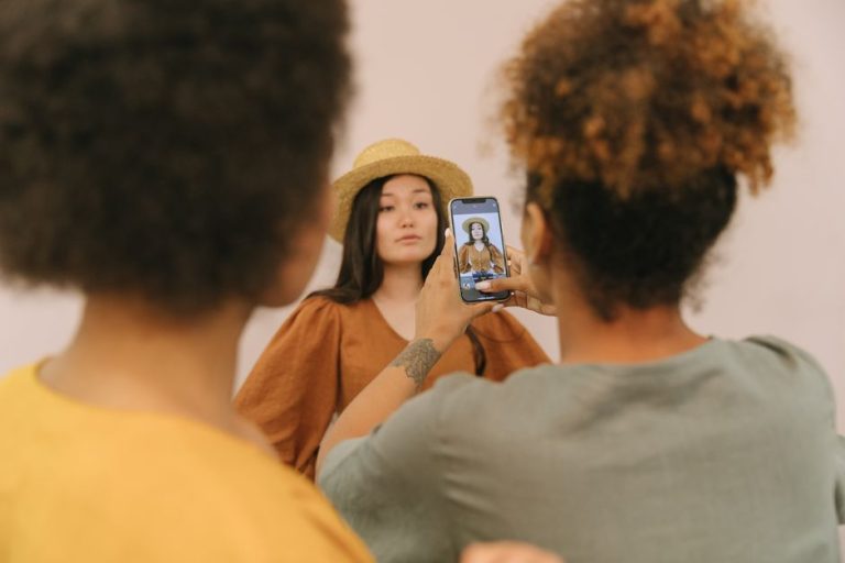 Model posing in a studio as an assistant takes a picture using a smartphone.