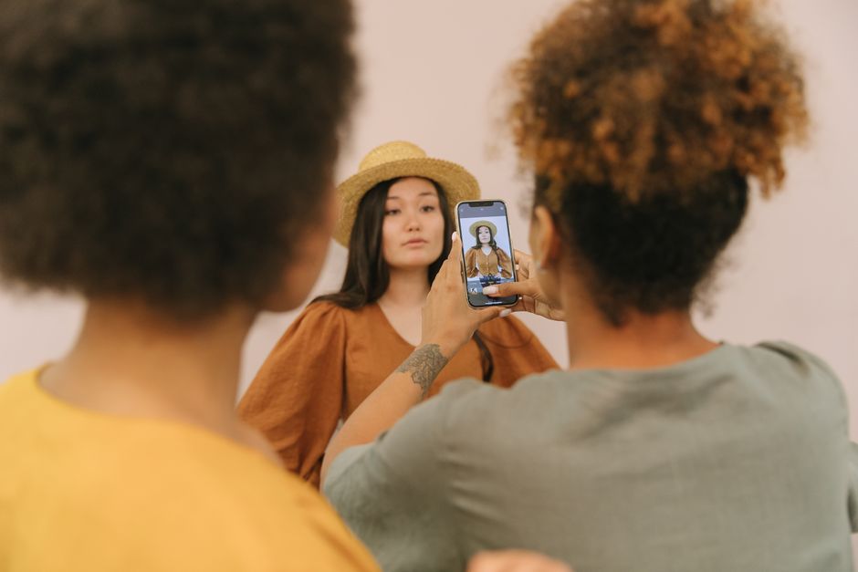 Model posing in a studio as an assistant takes a picture using a smartphone.