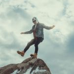 Balancing Individual Autonomy and Collective Cohesion | Strategy A man in casual attire balancing on a rock with a cloudy sky as a backdrop, exuding adventure.