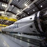 A SpaceX Falcon rocket displayed in a spacious hangar under bright industrial lights.