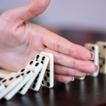 A close-up of a hand stopping a row of falling dominoes to illustrate strategy and control.