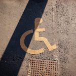 Beyond Compliance: Why 'Design Thinking' is the New Healthcare Requirement Close-up of a yellow wheelchair symbol painted on asphalt, highlighting accessibility.