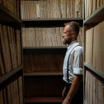 Beyond the Back Catalog: The 'Sovereign Artist' Pivot in the Creator Economy A man in formal attire and suspenders stands in an archive surrounded by documents.