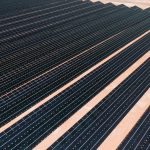 Aerial view of solar panels in a vast solar farm under bright sunlight.