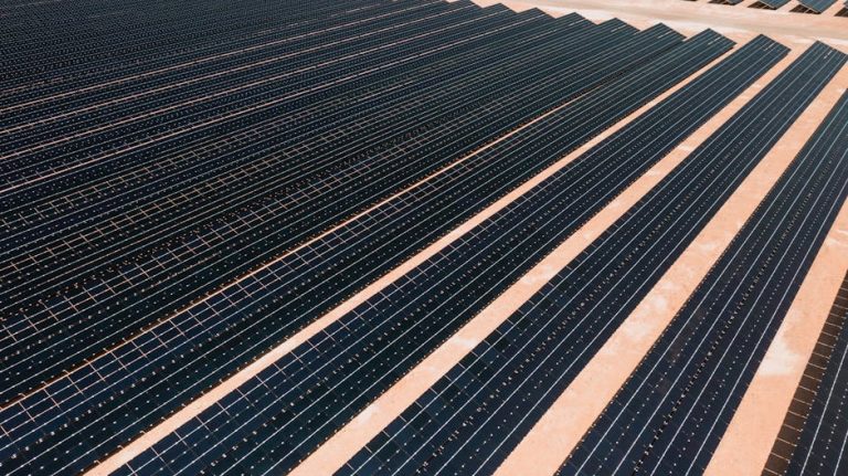 Aerial view of solar panels in a vast solar farm under bright sunlight.