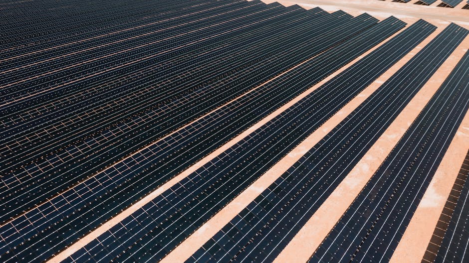 Aerial view of solar panels in a vast solar farm under bright sunlight.