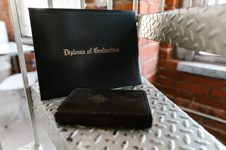 Close-up of a diploma and book on a metal staircase indoors, symbolizing academic achievement.