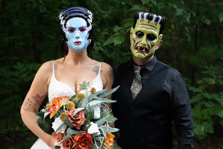 A couple in monster masks and wedding attire posing in a forest setting.