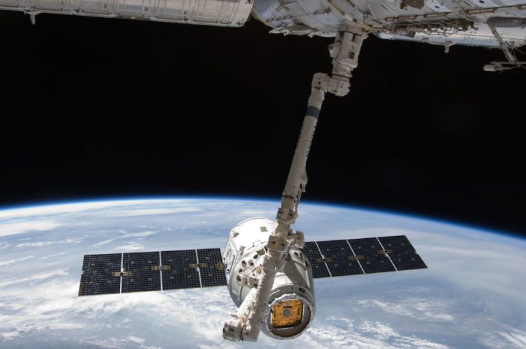 View of a spacecraft docked at the ISS above Earth with visible solar panels.