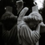 Beyond the Martyr Complex: Why Sustainable High-Performance Requires 'Creative Detachment' A reflective black and white photo of a solemn angel statue embracing a cross, evoking spirituality.