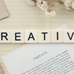 Close-up of letter tiles spelling 'Creative' on a lined notepad with decorative elements.