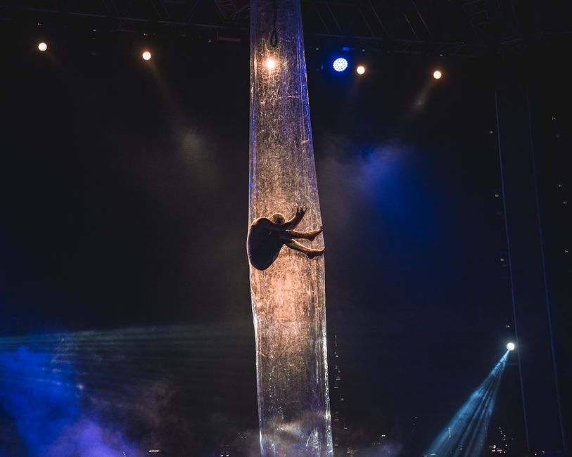 Aerial performer gracefully suspended on stage with dramatic lighting effects at night.