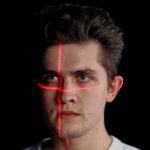 Conceptual portrait with laser scanning for facial recognition on plain black background.