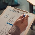 Person's hand holding a company invoice on a clipboard with a pen.